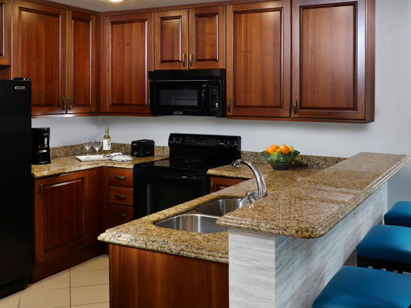 A modern kitchen with wooden cabinets, a microwave, stove/oven, granite counters, sink, and a bowl of oranges.