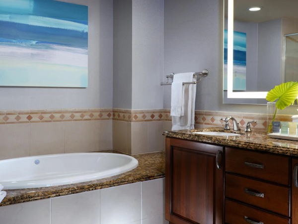 A modern bathroom with a white bathtub, granite vanity, towel racks, and beach-themed wall art near the shower.