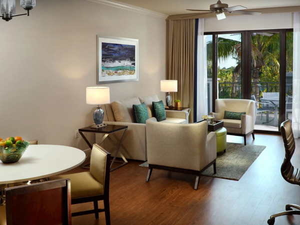 A bright modern living room with sofas, lamps, a round dining table, and large sliding doors opening to a tropical balcony.
