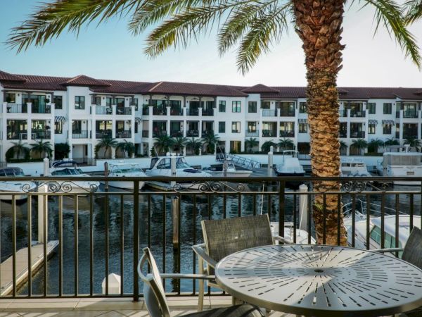 Balcony view of a waterfront hotel with a palm tree, railings, and moored boats on the canal under a blue sky.