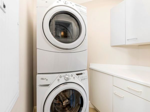 A stack of white front-loading washing machines/dryers in a clean utility room.