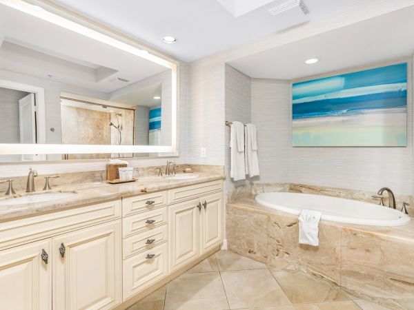 A bright modern bathroom with a double vanity, large mirror, framed art, and an oval soaking bathtub with towels.