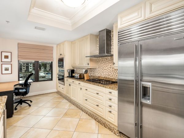Bright modern kitchen with cream cabinets, granite counters, tiled backsplash, gas stove, and a stainless fridge and double sink.