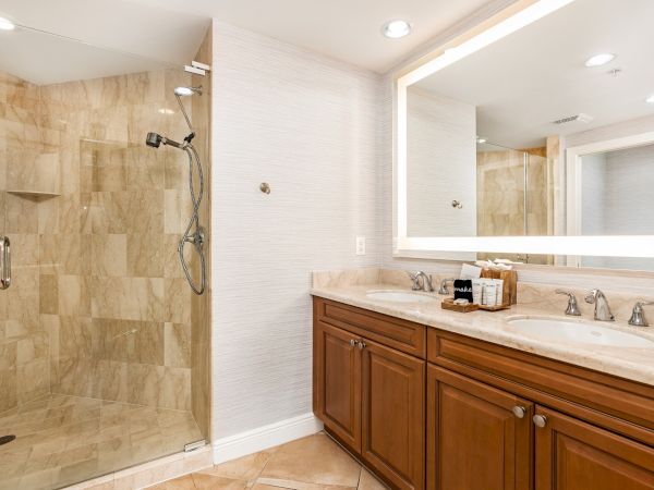 A modern bathroom with a marble-tiled walk-in shower, rainfall showerhead, double sinks, and warm wood vanity cabinets.