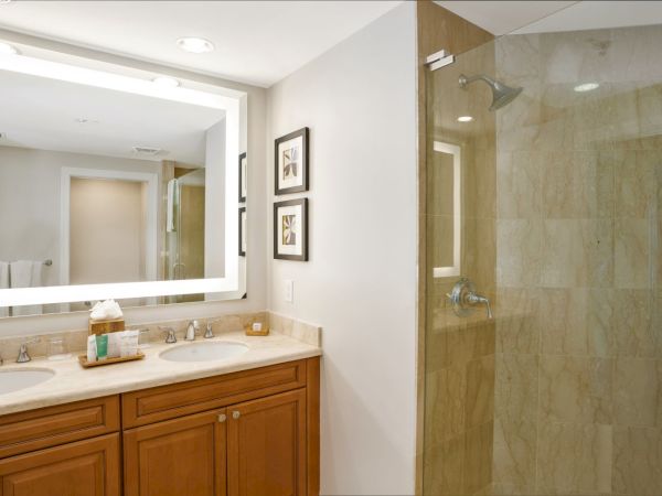 A bright modern bathroom with a double sink vanity, framed mirrors, and a glass shower with a showerhead.
