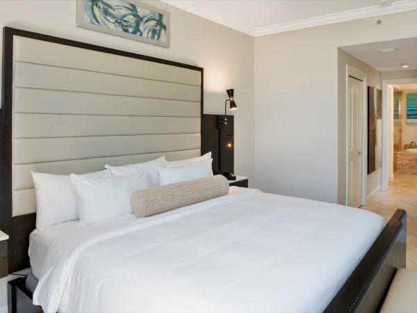 A modern hotel bedroom with a king bed, nightstands, wall art, and an open doorway to a tiled bathroom.
