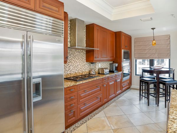 A modern kitchen with wood cabinets, tiled backsplash, stainless fridge, stove, and a breakfast table with stools.
