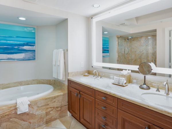 A bright luxury bathroom with a soaking tub, double vanity, stone walls, and a large mirror over a shower.