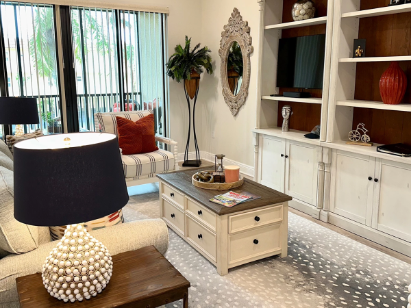 Cozy living room with a beige sofa, round black lamps, a wooden coffee table, built-in white cabinets, shelves, a wall mirror, and a rug.