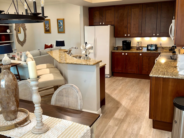 A modern open-concept kitchen and dining area with granite countertops, dark wood cabinets, a small breakfast bar, and a living room nook.
