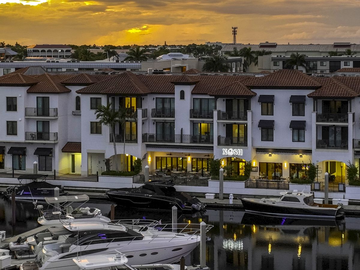 A sunset over a marina with moored yachts in front of a white hotel complex with terracotta roofs.