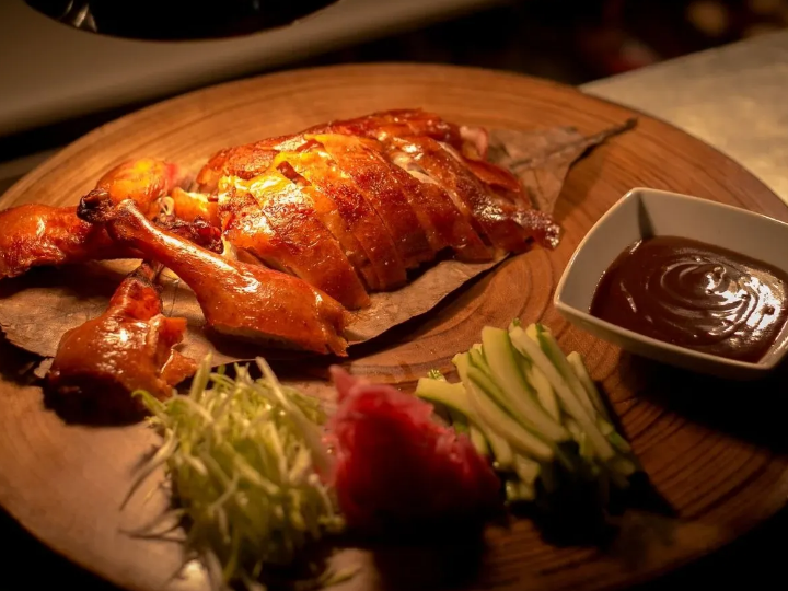 Roasted chicken on a wooden board with fresh greens, radish, and a bowl of dark dipping sauce.