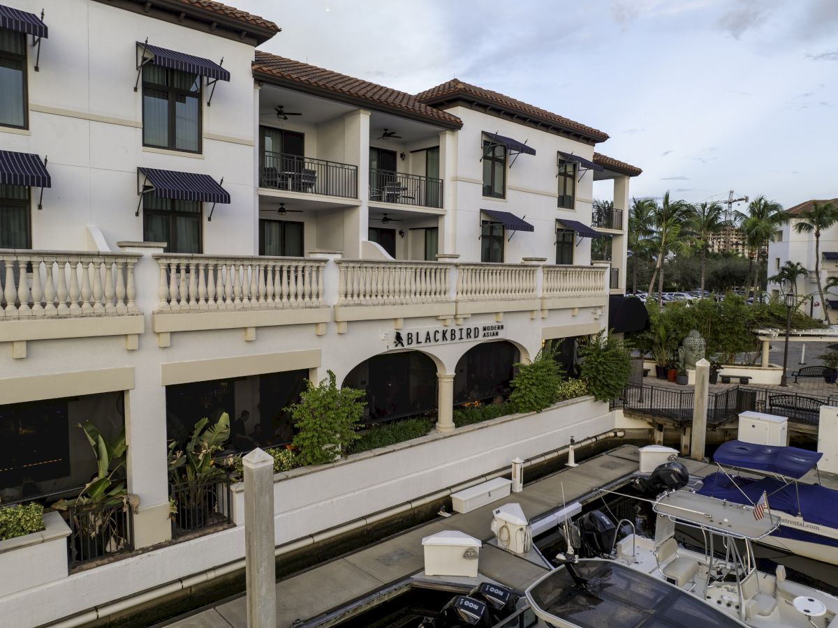White hotel building with red-tile roof, blue awnings, balconies, a courtyard with palms, and &ldquo;Blackbird&rdquo; sign below.