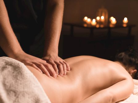 A person receiving a relaxing massage on a spa bed, with warm candle lights glowing in the softly blurred background.
