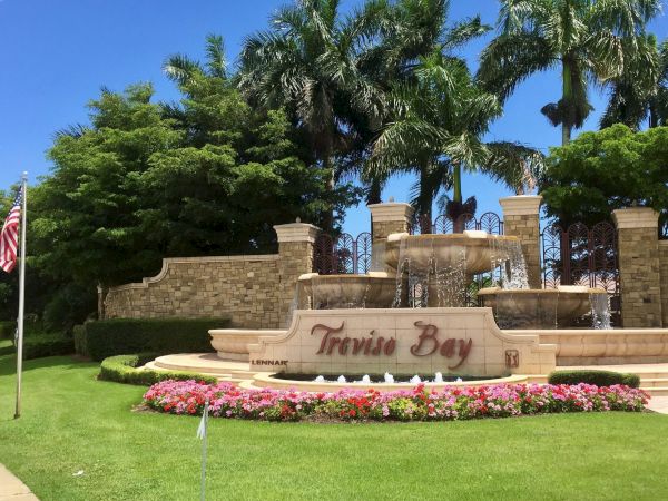 Sunlit resort scene with palm trees, a rock fountain, colorful flowers, and a &ldquo;Travis Bay&rdquo; sign with a U.S. flag.
