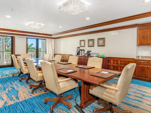A spacious boardroom with a long wooden table, beige swivel chairs, built-in wooden cabinetry, and a bright blue patterned carpet.