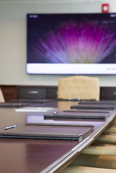 A conference room with a long table, chairs, notebooks, and a wall-mounted monitor showing colorful graphics.