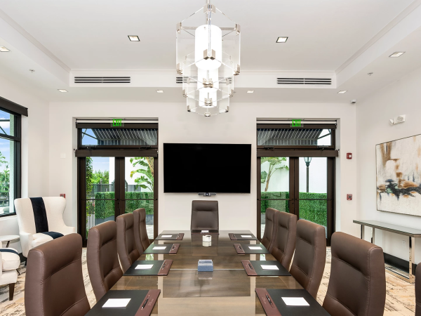 A modern conference room with a long table, brown chairs, a wall-mounted TV, large windows, and elegant lighting.