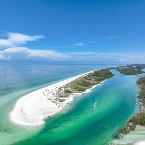 Aerial view of a tropical beach with turquoise water, boats, and a curving lagoon under a blue sky.