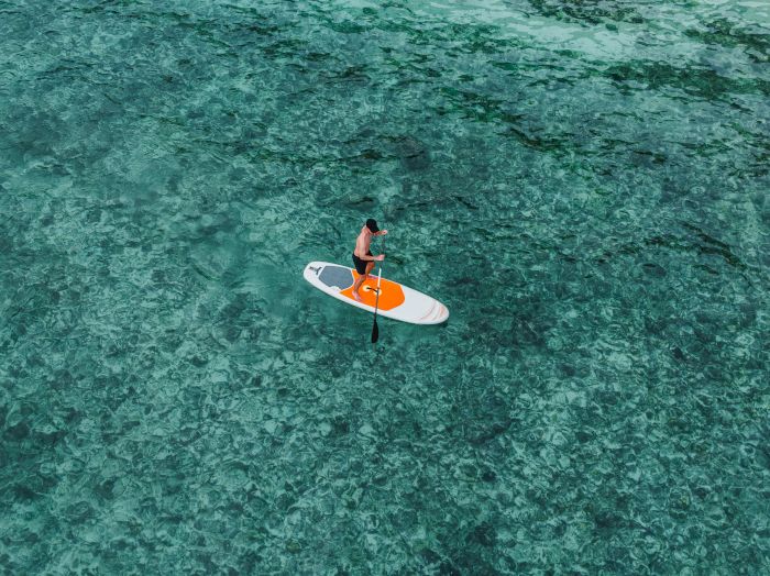 A person paddleboards on clear turquoise water, standing and paddling steadily with an orange-and-white board.