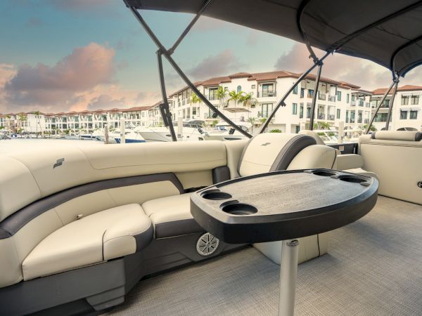 A luxurious boat deck with cream seating, a circular table, cup holders, and panoramic marina views in the background, under a canopy.