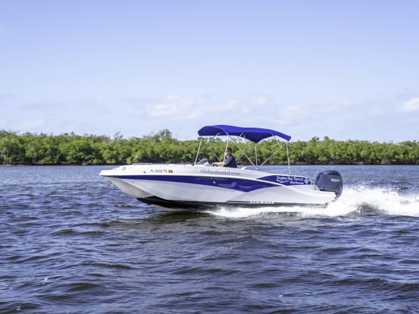 A sleek white speedboat with a blue stripe glides across calm water, a blue canopy overhead, leaving white spray as it races by.