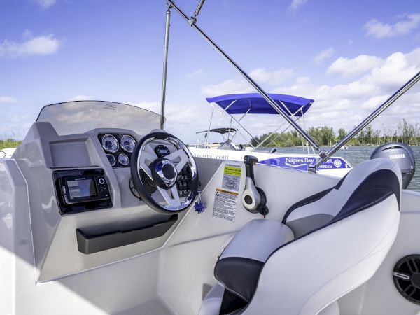 A modern boat cockpit with a steering wheel, gauges, captain seat, and a blue canopy on a sunny day, ready for cruising.