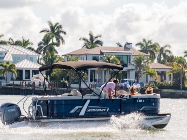 A motorboat cruising on calm water near waterfront houses with palm trees in the background, people riding and enjoying the ride.