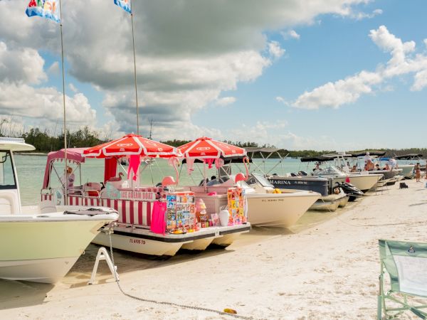 Colorful beach boats with pink-striped canopies docked along a sandy shoreline under a bright, partly cloudy sky.