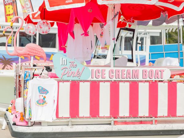 A pink and white ice cream boat with striped sides, pink umbrellas, flamingo decor, and a playful pastel theme.