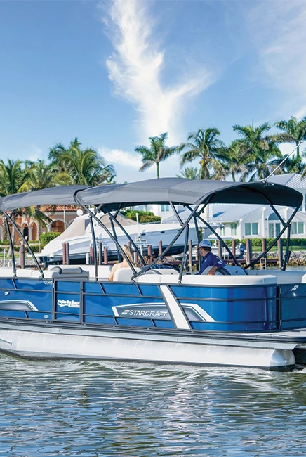 A blue pontoon boat with a canopy cruising on calm water, palm trees and resort buildings lining the shore.