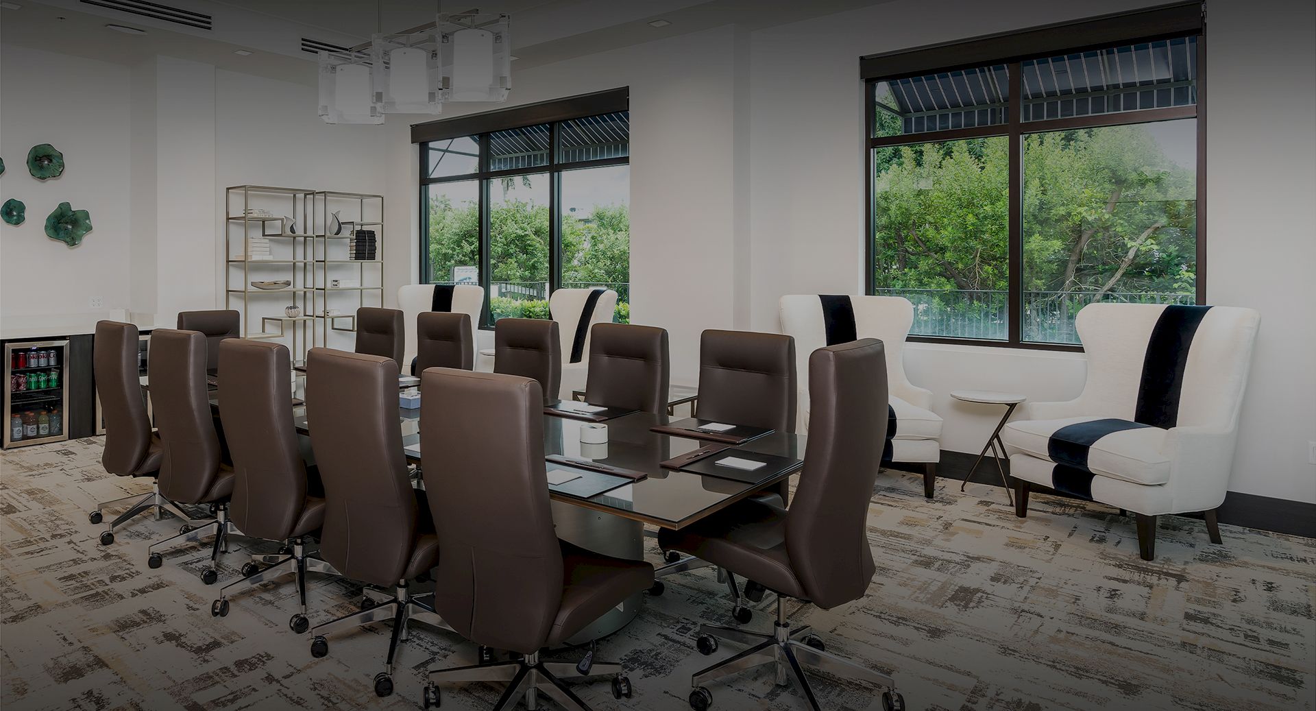 A modern conference room with a long table, brown ergonomic chairs, large windows, and white lounge chairs by the wall; professional workspace.
