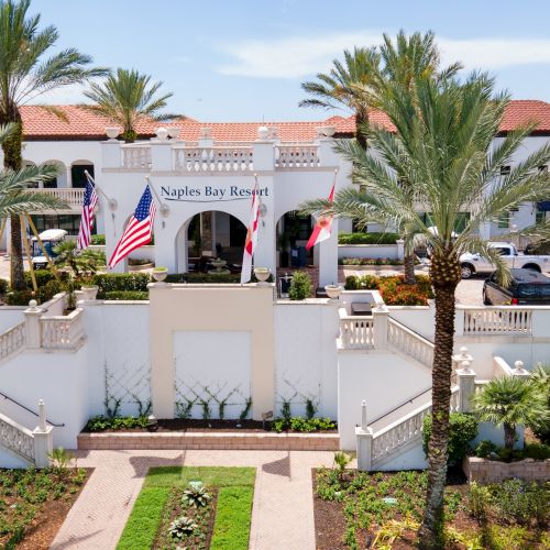 Naples Bay Resort hotel entrance with palm trees and flags in front of a white building.