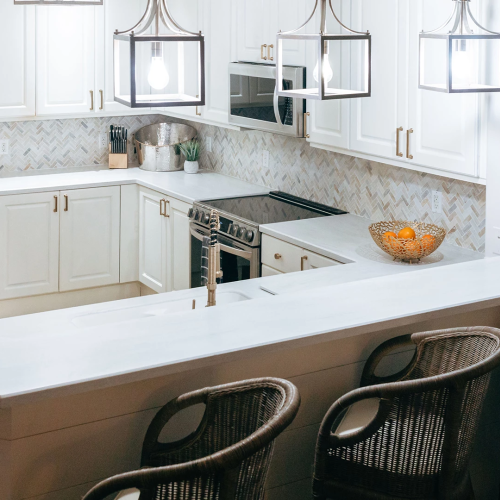 Bright modern kitchen with white cabinetry, an island, pendant lights, a stainless range, and bar stools in view.