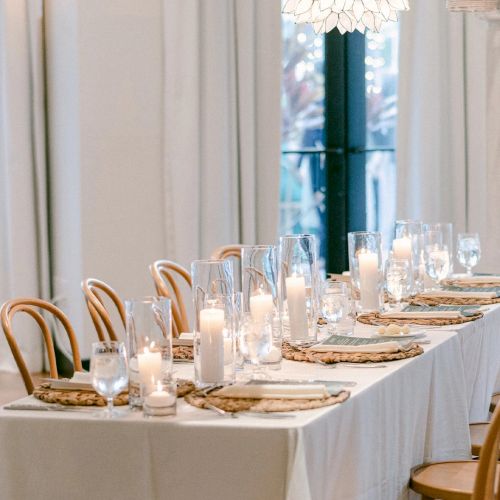 An elegantly set banquet table with candles, glassware, and cutlery in a bright indoor event space.