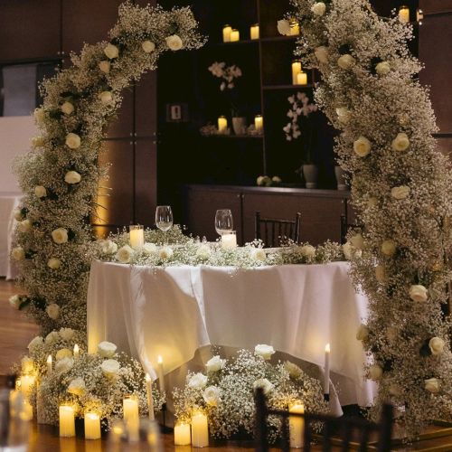 A beautifully decorated wedding table surrounded by white baby&rsquo;s breath, soft candles, and warm lights in a dark reception hall.
