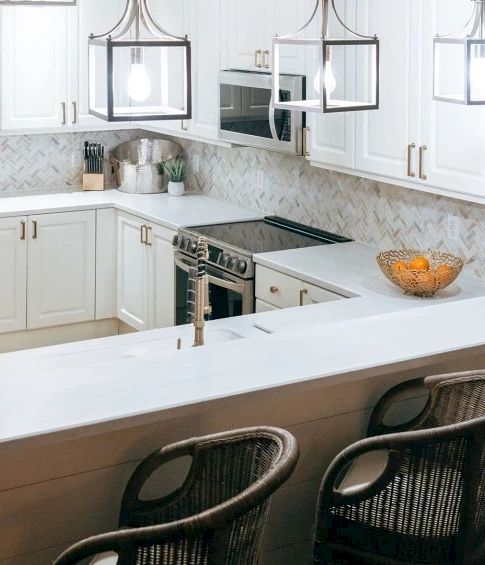 A bright white kitchen with cabinetry, a stainless range, pendant lights, and a large white island with bar stools.