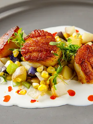 A plate of grilled pork chops with roasted potatoes, corn and mixed vegetables, topped with fresh herbs and sauce dots.