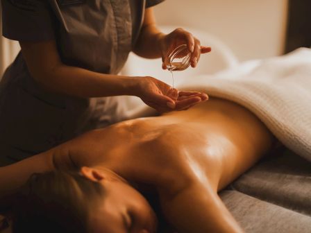 A therapist pours massage oil into their hands and oils a person&rsquo;s bare back during a relaxing massage, warm and intimate.