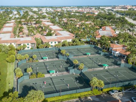 Aerial view of a tropical resort with palm trees, tiled villas, and multiple tennis courts beside the ocean.