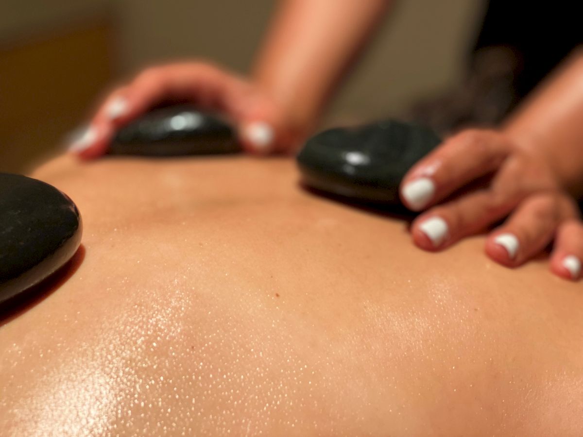 A close-up of an oil-and-stone massage as hands glide over a person&rsquo;s bare skin.