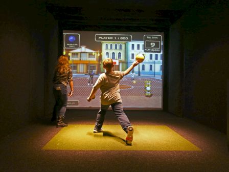 A boy in a batting stance plays an interactive baseball game on a screen in an arcade-style simulator.