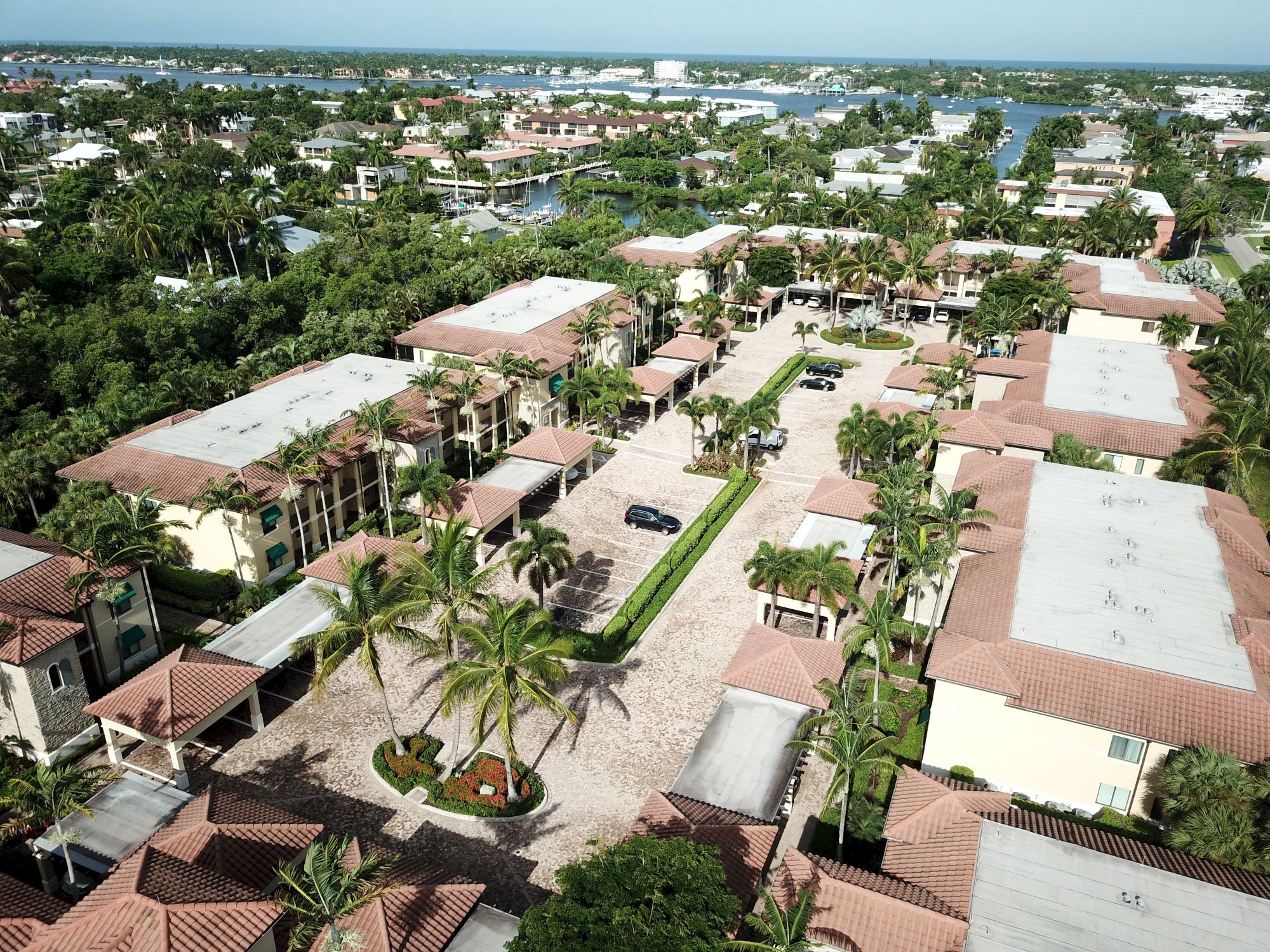 Aerial view of a tropical resort with palm trees, luxury villas, driveways, and a coastal ocean horizon.