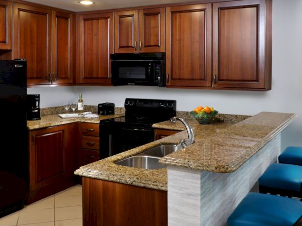Modern kitchen with wooden cabinets, granite counters, sink, stove, and microwave in a bright apartment, featuring bar seating.