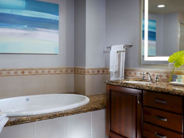 A modern bathroom with a white soaking tub, dark wood vanity, wall art, towels, and a glass-enclosed shower.