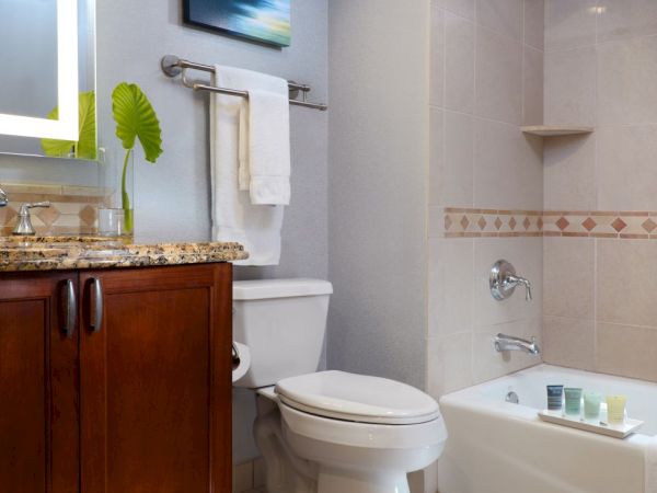 A modern bathroom with a vanity, toilet, bathtub, tiled walls, and towels with a decorative green plant.